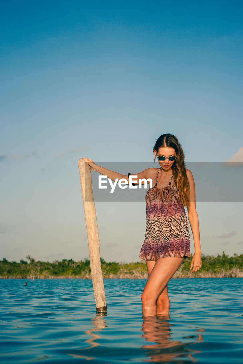 Young woman wearing sunglasses while standing in sea against sky