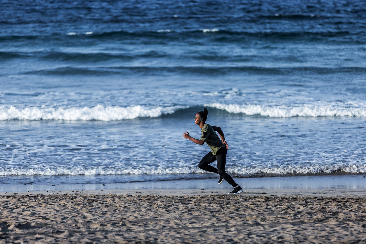 Side view of young man running at beach