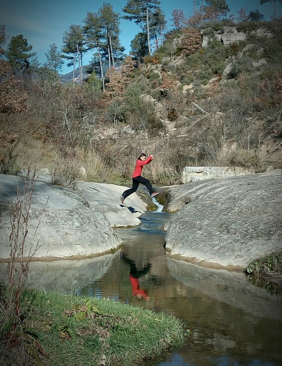 Man jumping from rock formation over stream