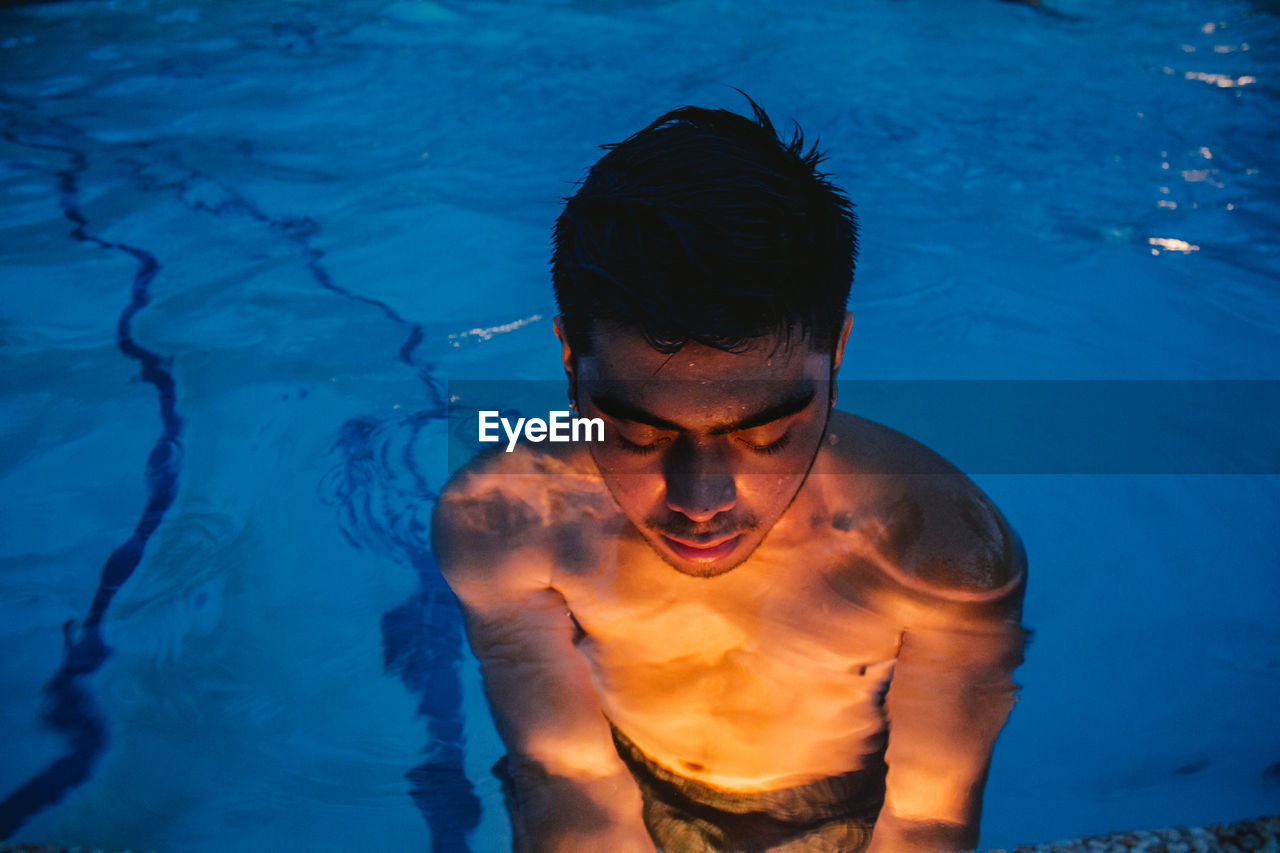 Young man in illuminated swimming in pool