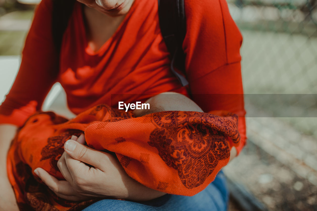 Midsection of woman breastfeeding baby outdoors