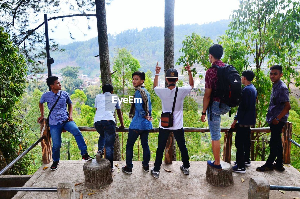 REAR VIEW OF MEN STANDING AGAINST TREES