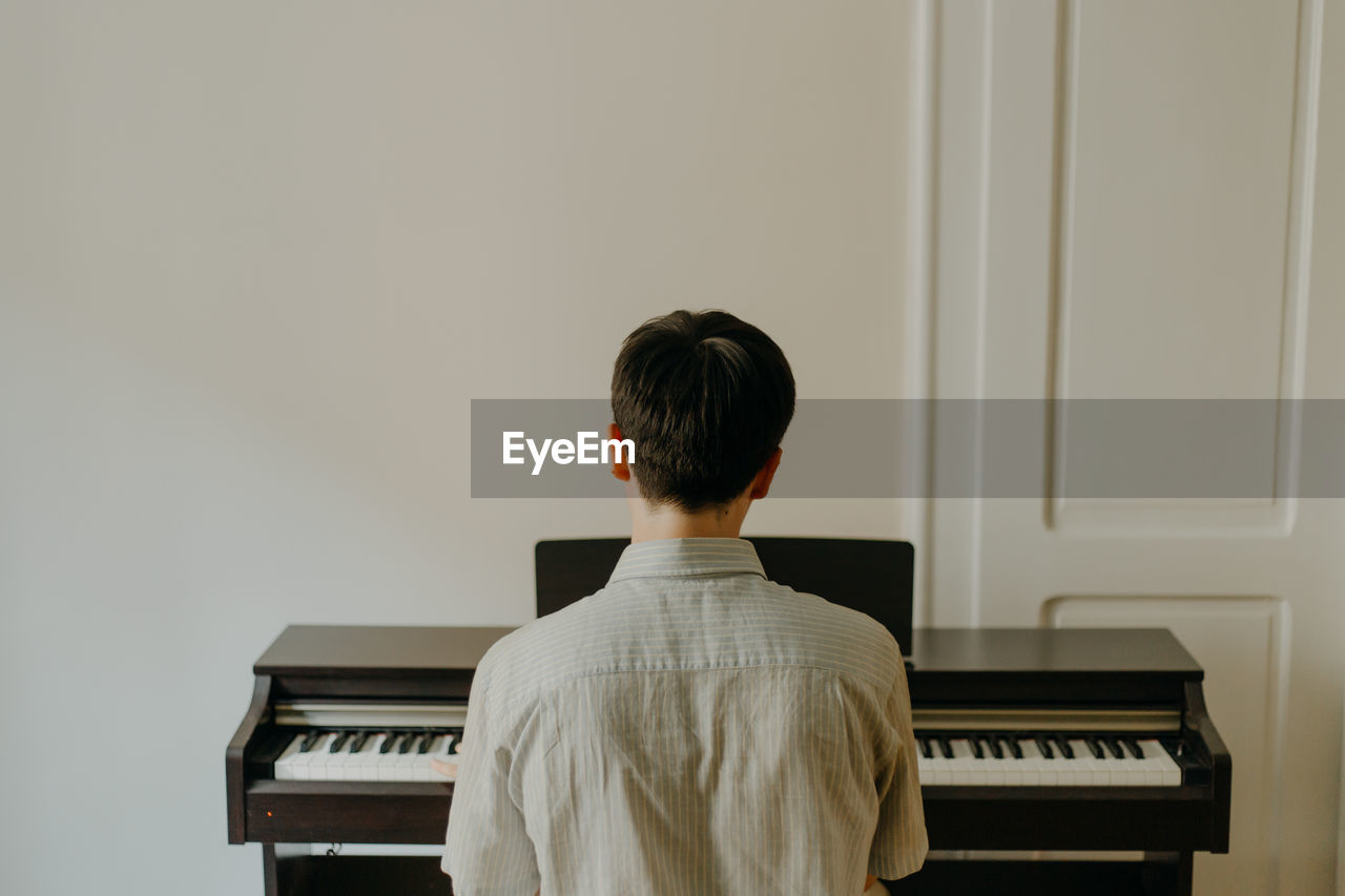 Rear view of a young man playing piano