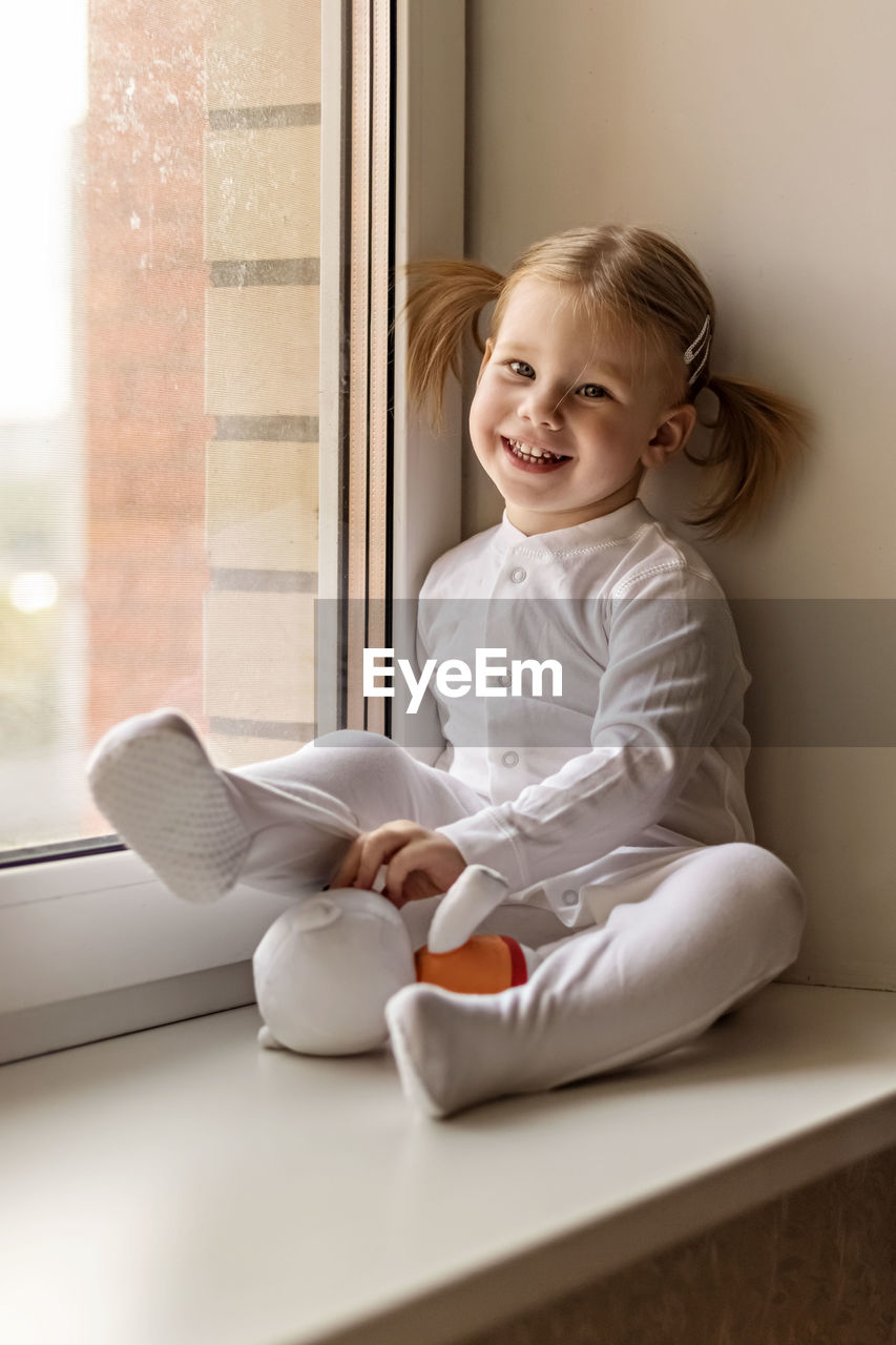 Full length of girl with stuffed toy sitting by window