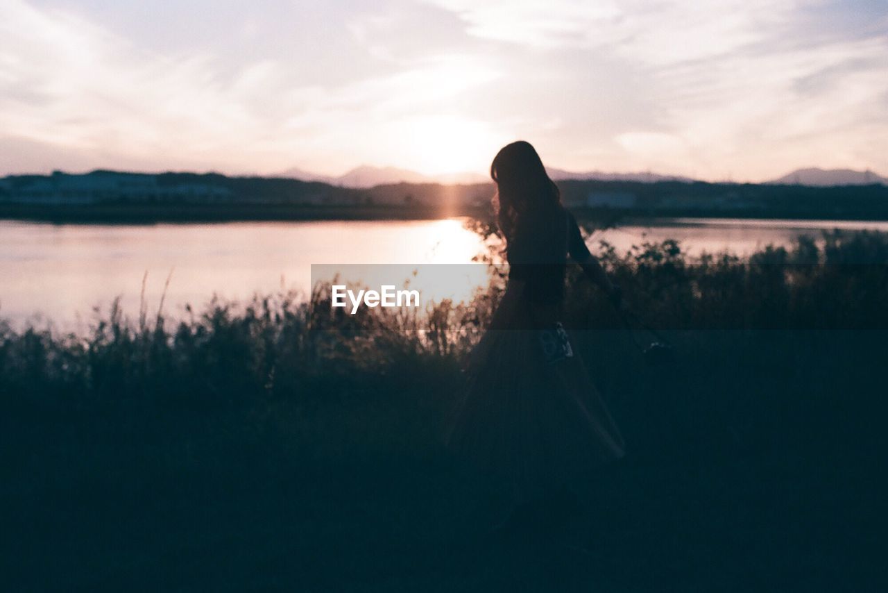 Full length of woman walking at lakeshore against sky during sunset