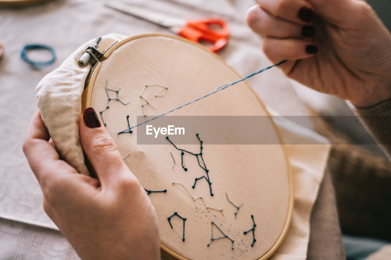 Side view of crop female with hoop and threads embroidering star constellations while sitting at table in light workshop