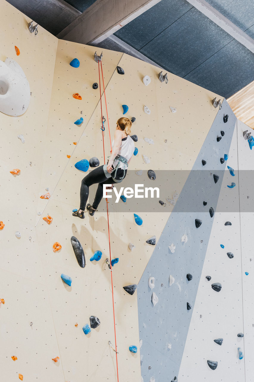 Back view full body of unrecognizable sportive female in activewear climbing on wall with grips during training in modern gym