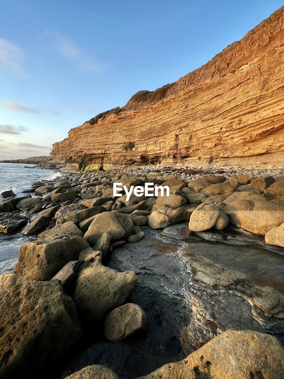 rock, land, sky, nature, scenics - nature, sea, water, landscape, coast, beauty in nature, environment, geology, shore, cliff, no people, travel destinations, beach, rock formation, travel, wadi, wilderness, terrain, tranquility, non-urban scene, outdoors, mountain, ocean, tranquil scene, natural environment, day, sunlight, clear sky, cloud, blue, formation, tourism, sunny