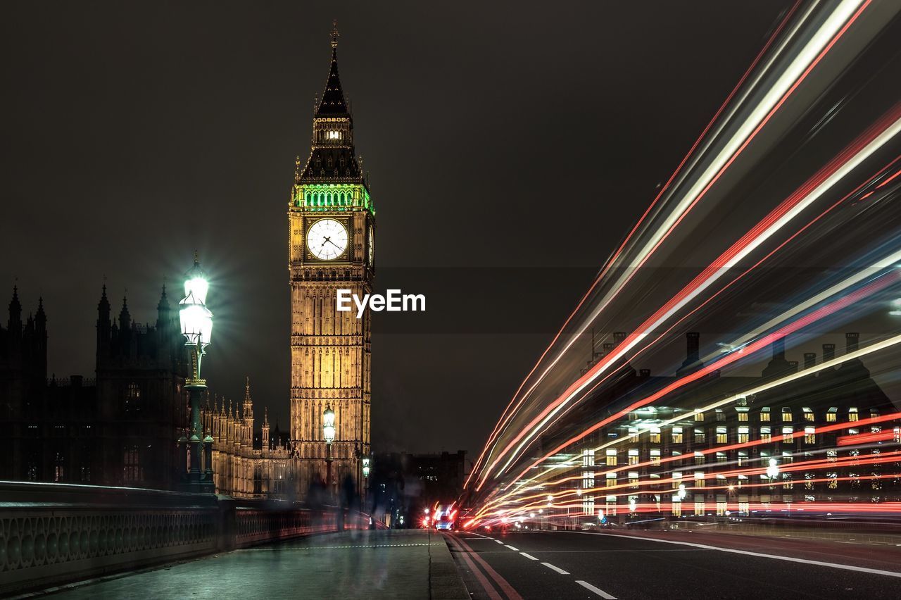 Light trails on city street by illuminated big ben against clear sky at night