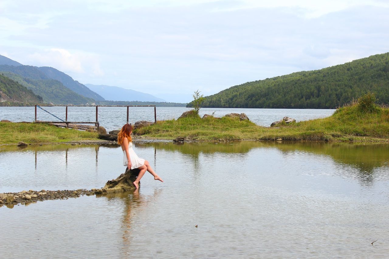 Woman sitting on rock at lakeshore against clear sky