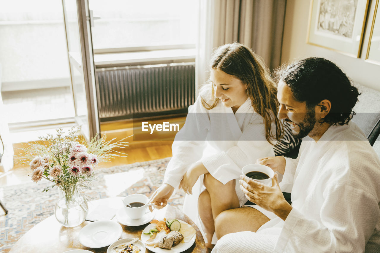 High angle view of couple in bathrobes enjoying breakfast at hotel room