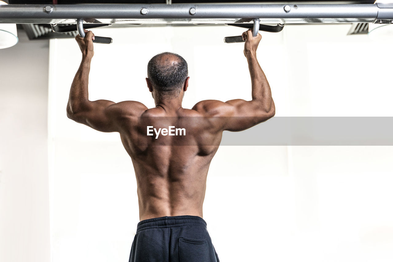 Rear view of shirtless man exercising in gym