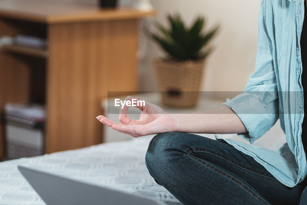 Midsection of woman meditating at home