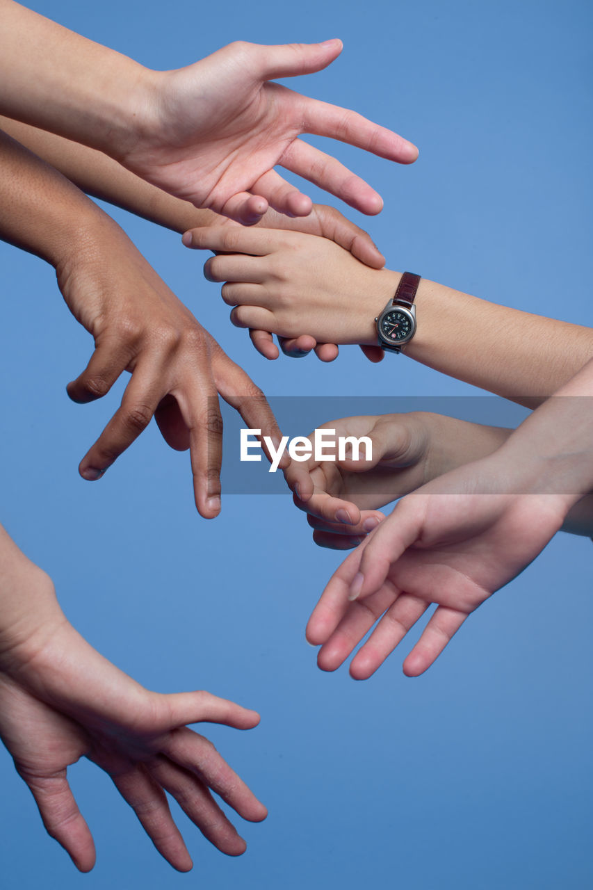 Cropped hands of people against clear blue sky