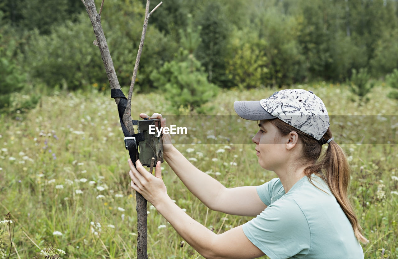 SIDE VIEW OF A YOUNG WOMAN HOLDING SUNGLASSES ON LAND