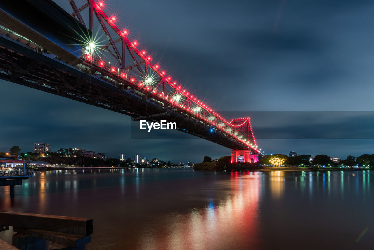 Illuminated bridge over river against sky at night