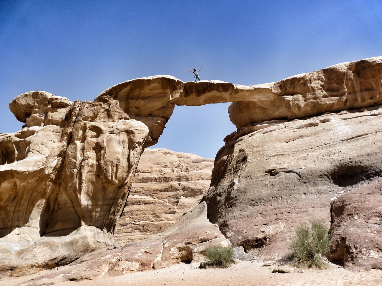 Low angle view of man standing on rock formation against clear blue sky