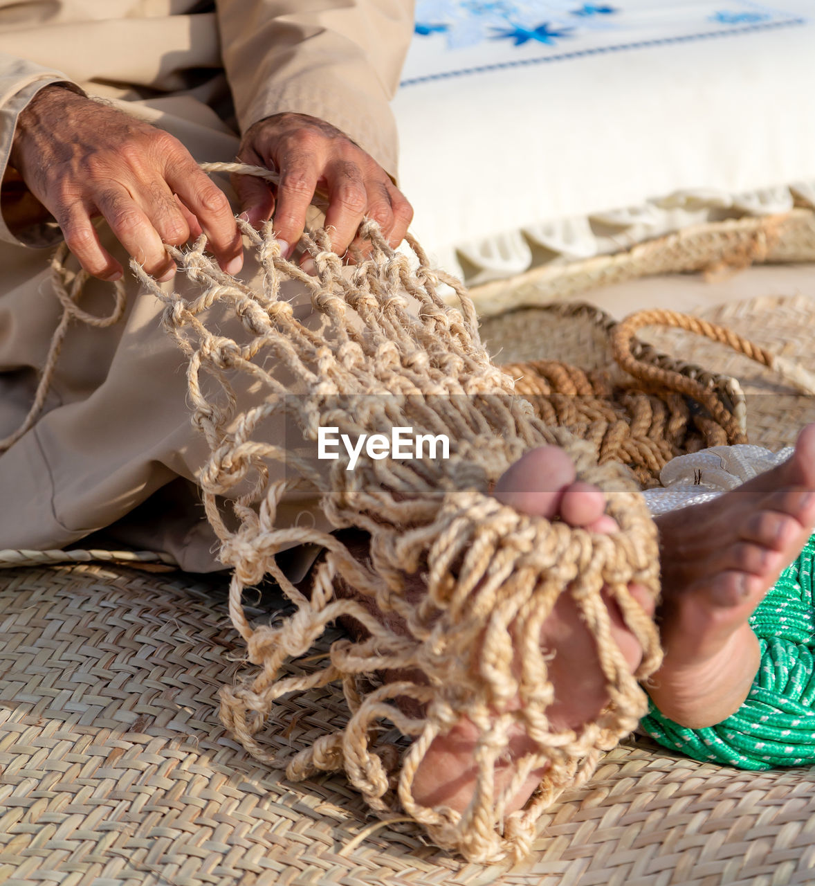 Old man is knitting traditional fishing net, hands and feet in frame