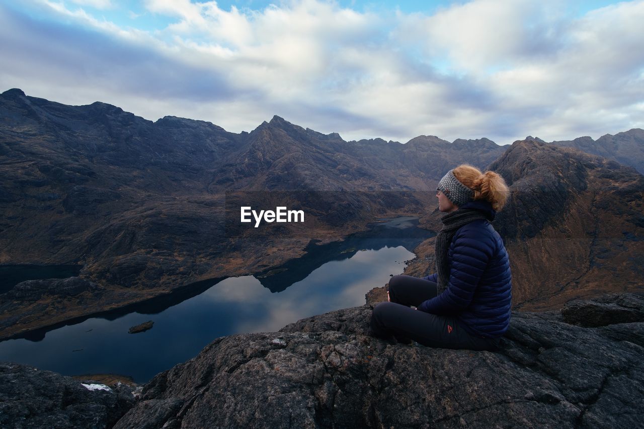 Woman sitting on rock by lake against sky