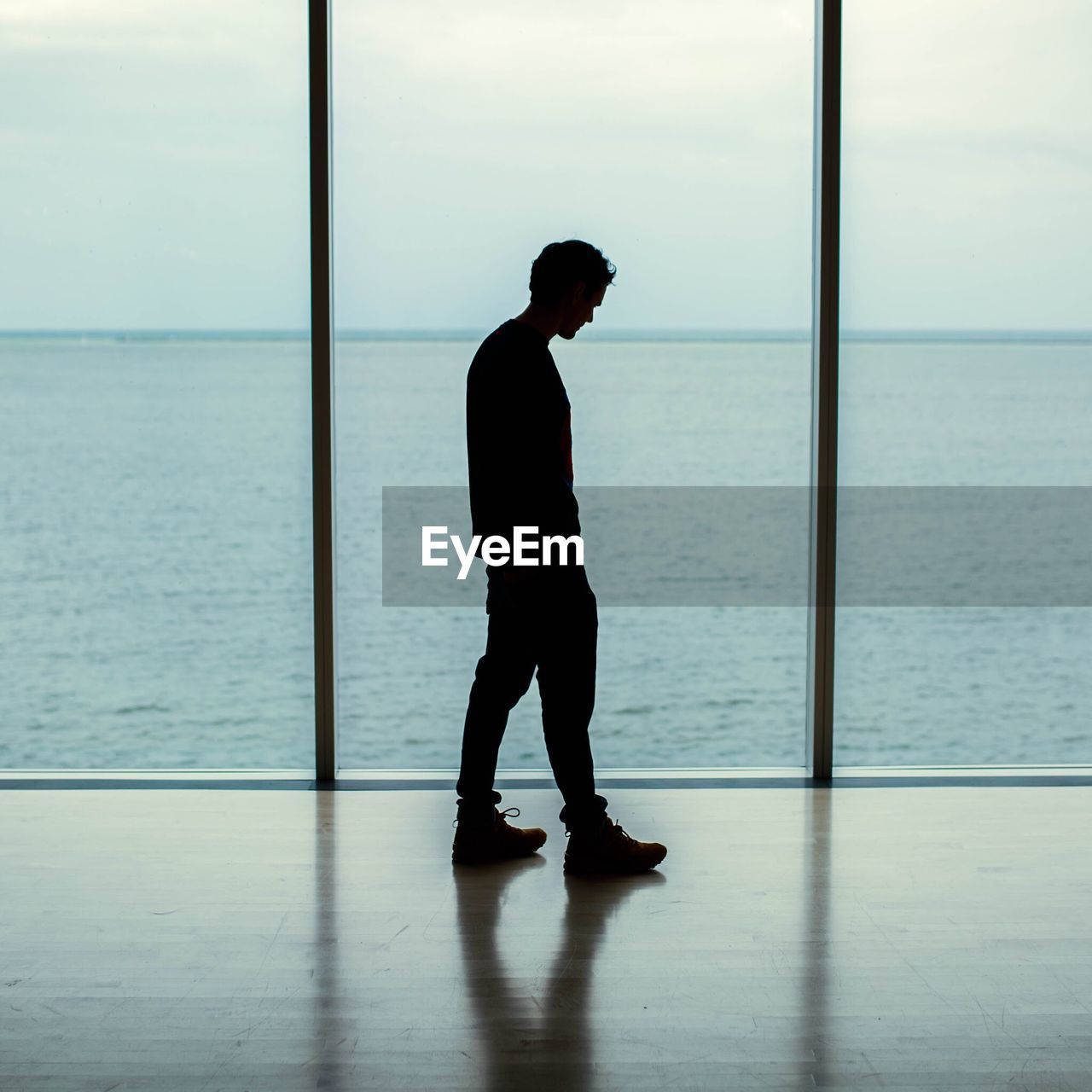 Side view of man standing with sea seen through window