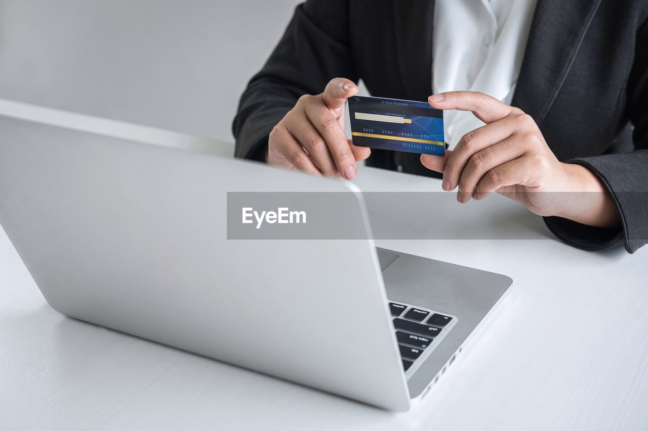 Midsection of businesswoman holding credit card by laptop on table