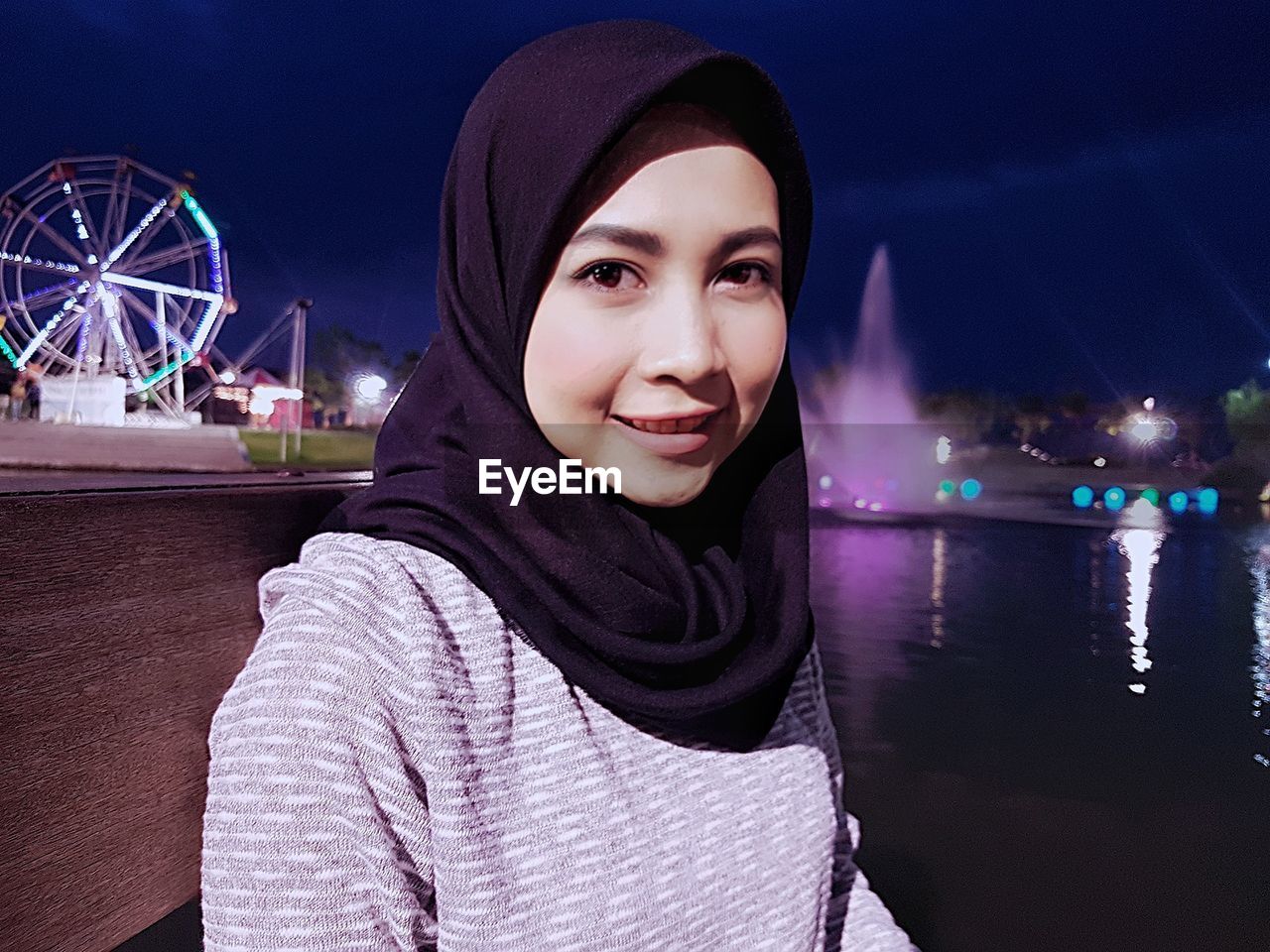 Portrait of smiling young woman against sky at night