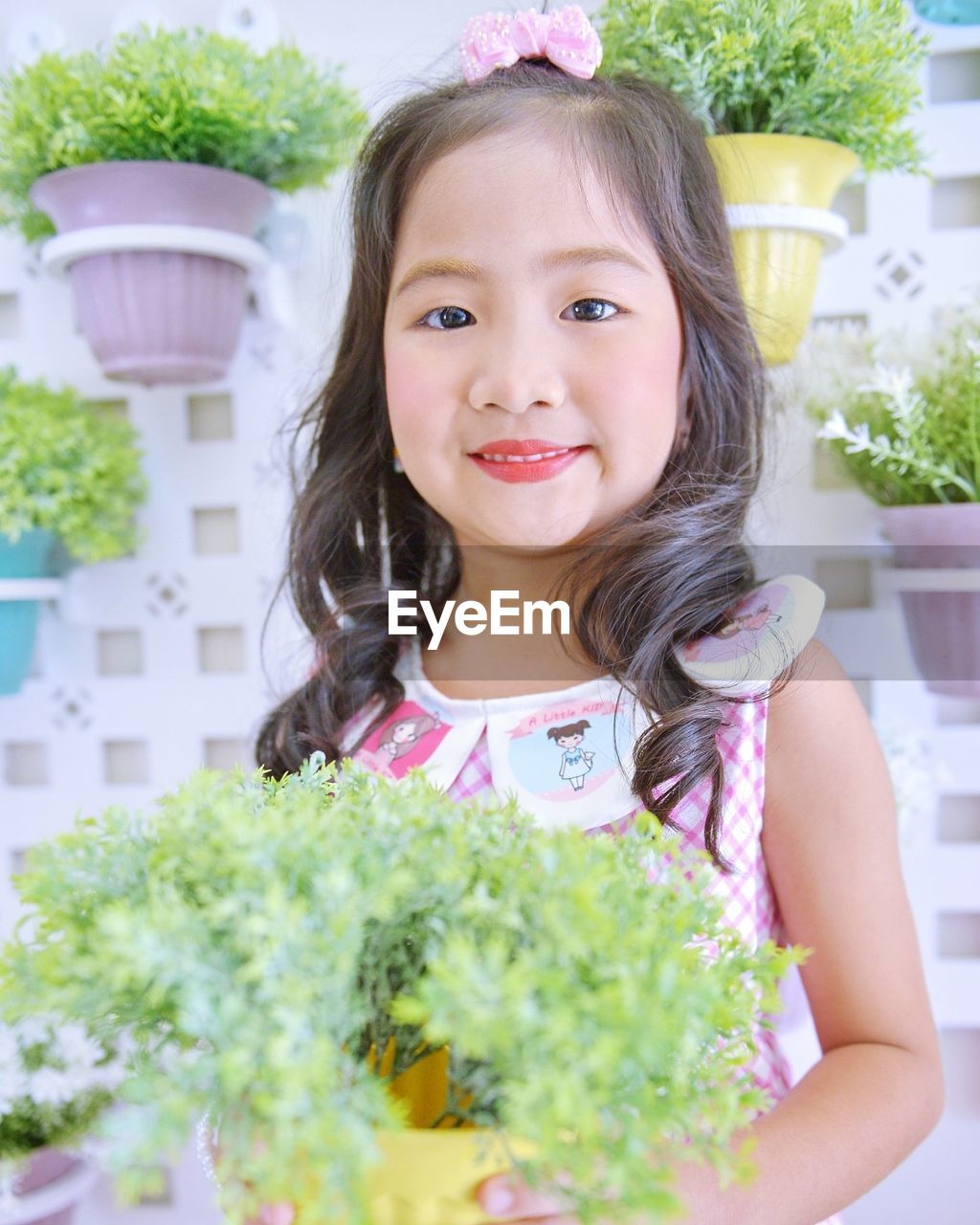 CLOSE-UP PORTRAIT OF SMILING GIRL WITH POTTED PLANTS