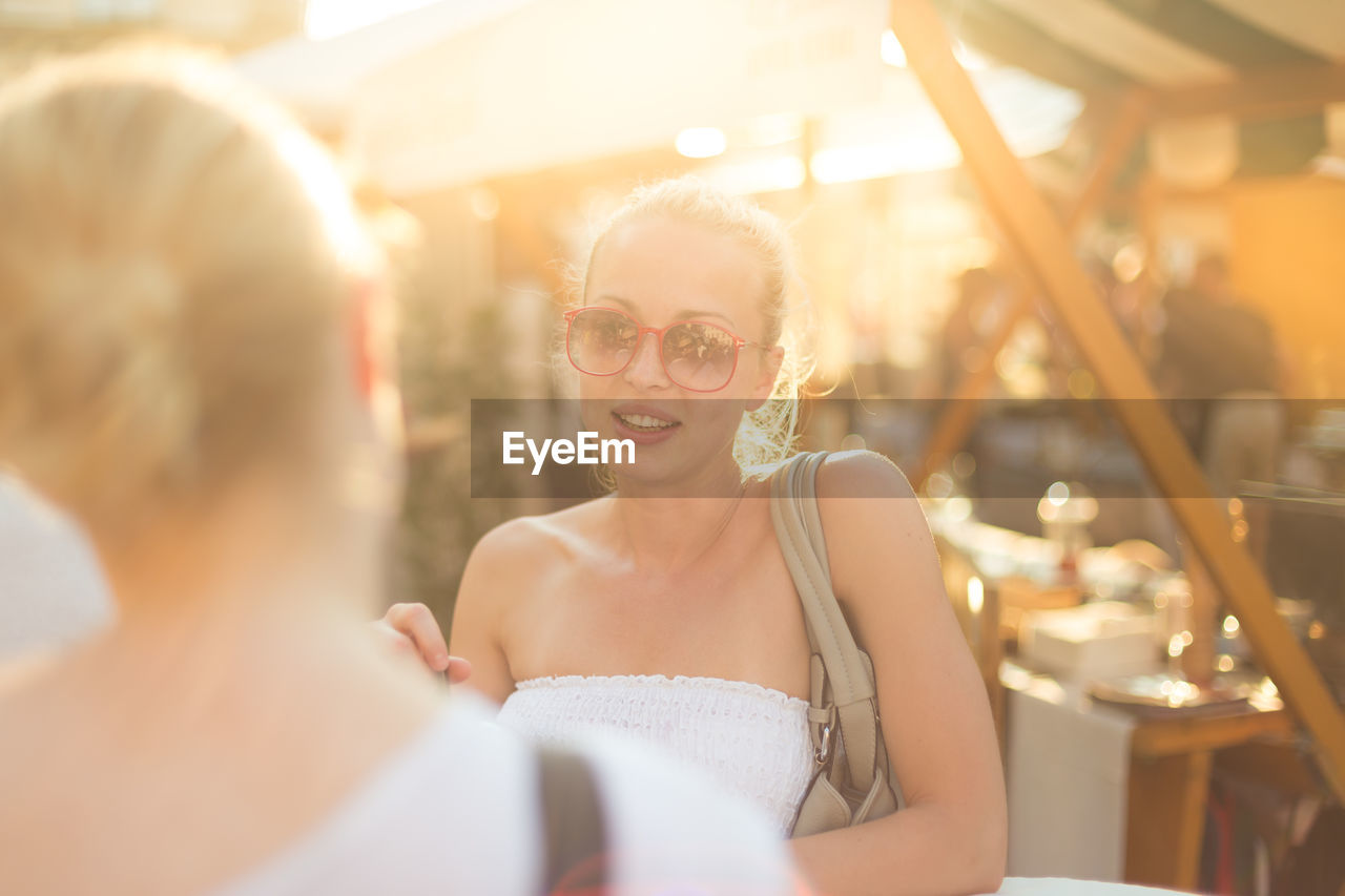 Smiling woman talking with friend sitting at cafe outdoors