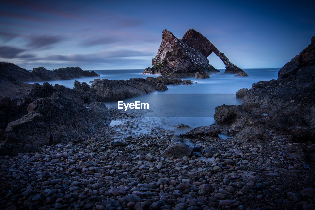 Scenic view of rock formations in sea against sky at dusk