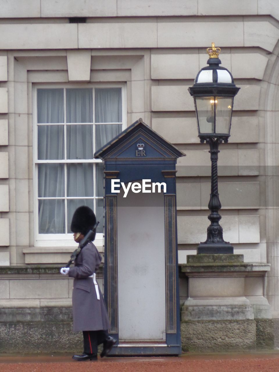 REAR VIEW OF WOMAN STANDING BY STREET LIGHT AGAINST BUILDING IN CITY