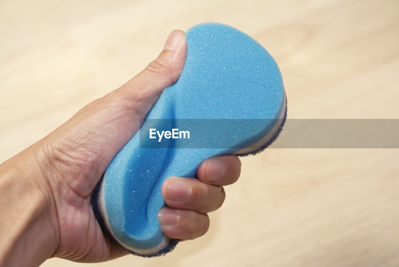 Cropped hand of man holding sponge over wooden table