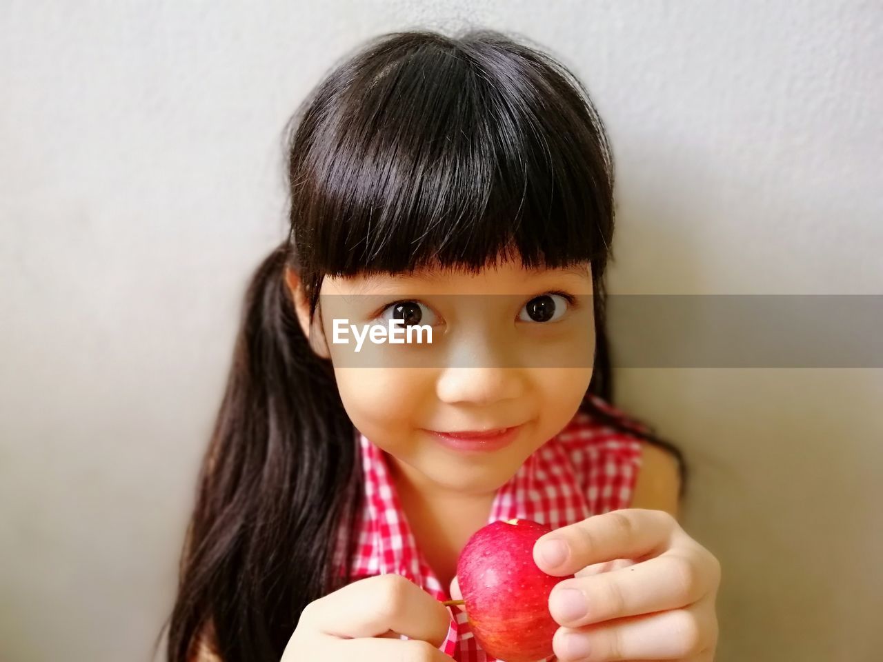 Portrait of cute girl holding apple while sitting against wall