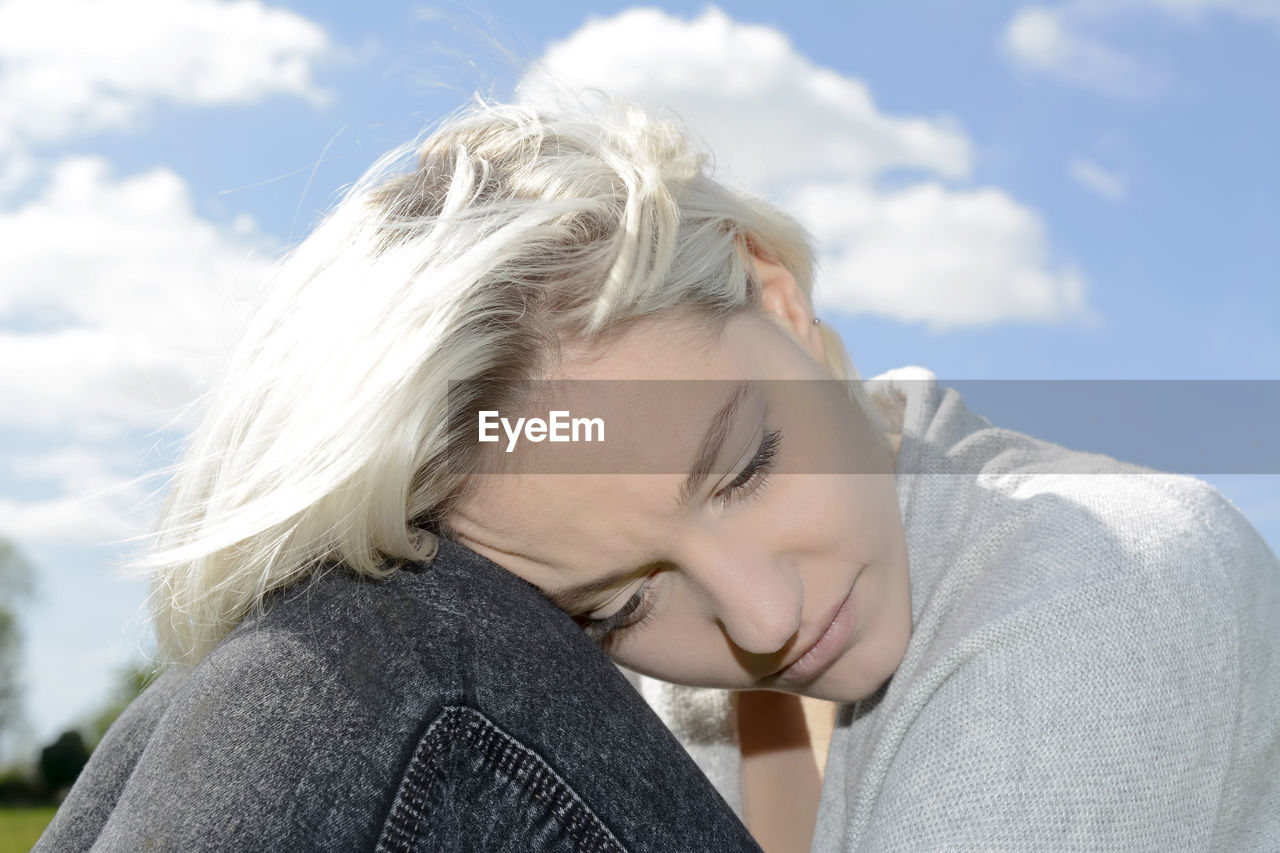 Close-up of sad woman looking down against sky