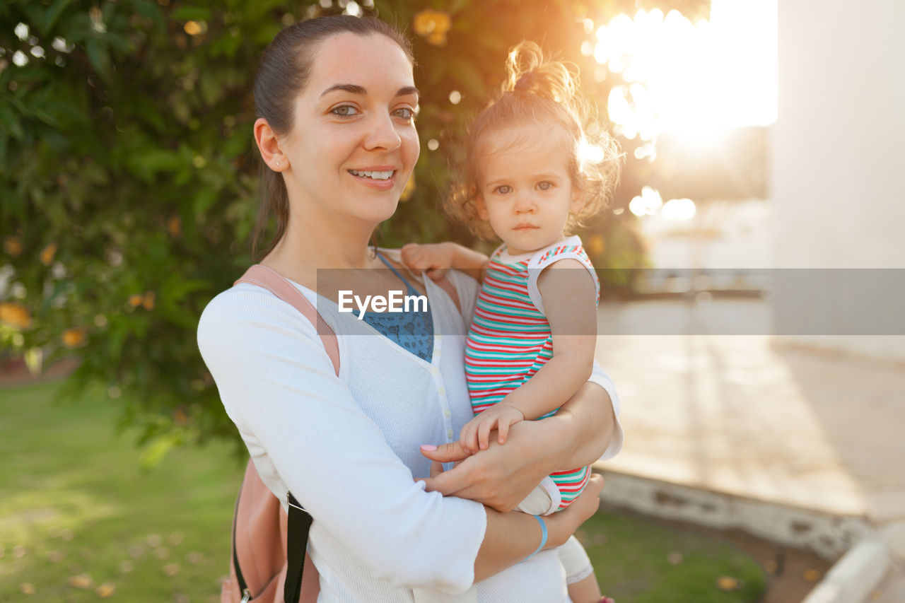 Portrait of mother carrying cute daughter while standing in park