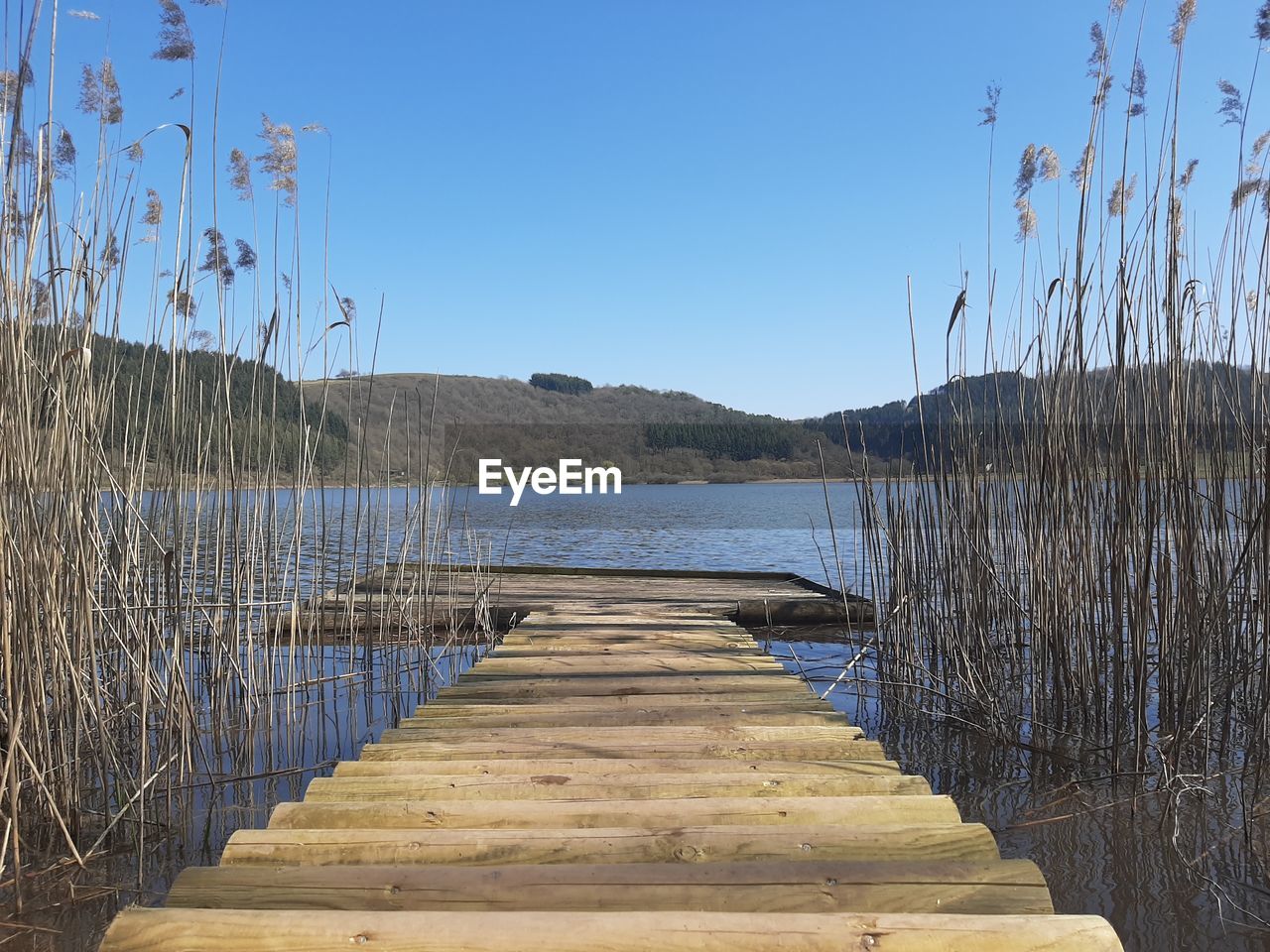 Pier over lake against clear blue sky