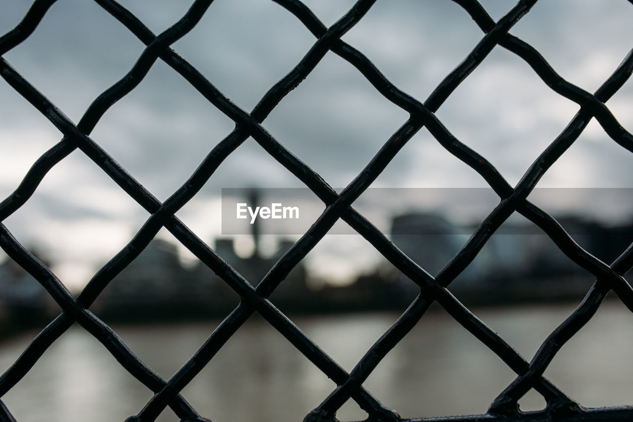 FULL FRAME SHOT OF CHAINLINK FENCE AGAINST BLURRED BACKGROUND SEEN THROUGH METAL