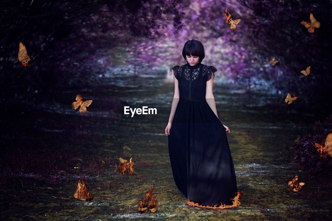 Digital composite image of woman wearing dress walking on pathway amidst burning butterflies