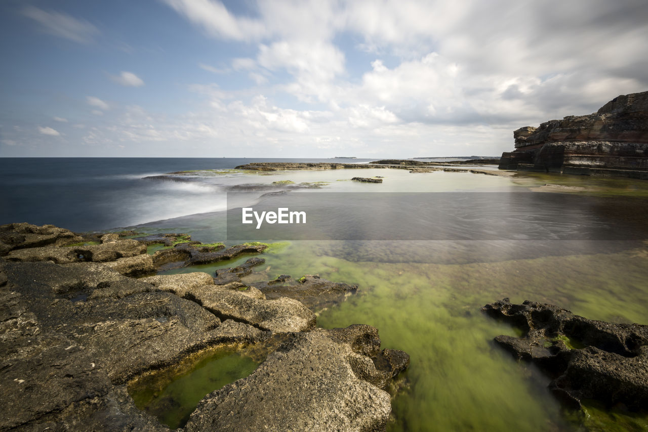 Scenic view of rock formation by seascape against cloudy sky