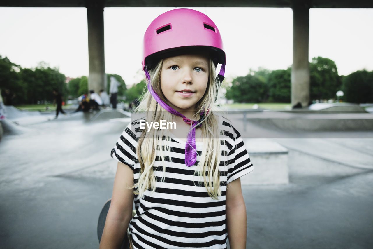 Portrait of smiling girl wearing pink helmet standing at skateboard park