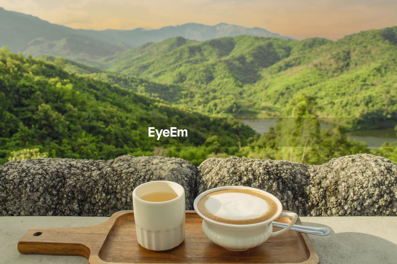 COFFEE CUP ON TABLE BY MOUNTAINS