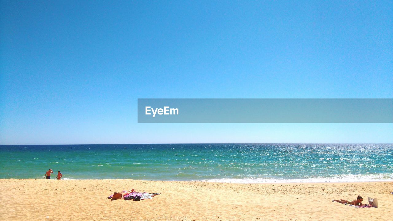 People on beach against clear blue sky