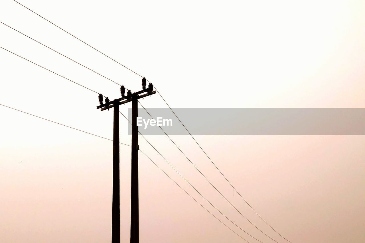 Low angle view of silhouette electricity pylon against clear sky