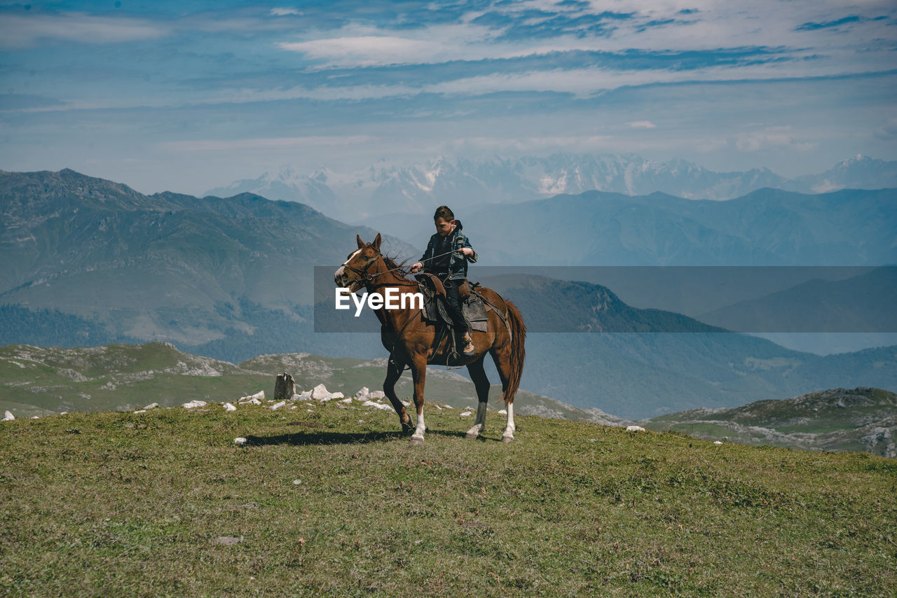Full length of boy sitting on horse against mountain