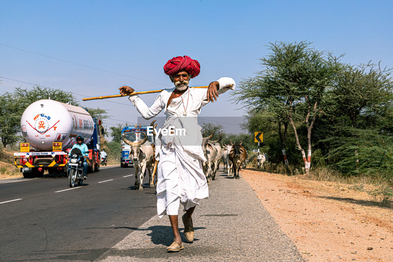 REAR VIEW OF MAN WALKING ON ROAD WITH TREES