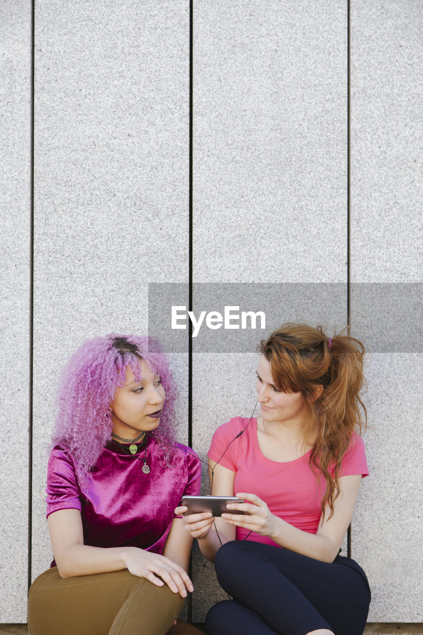 Lesbian couple looking at each other while sitting against wall