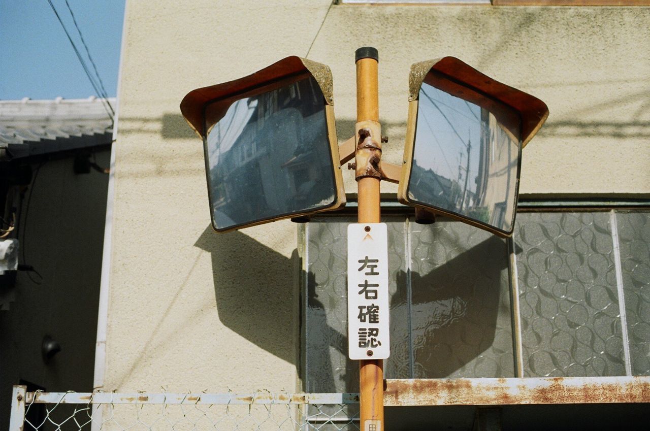 Low angle view of road mirror with text against building