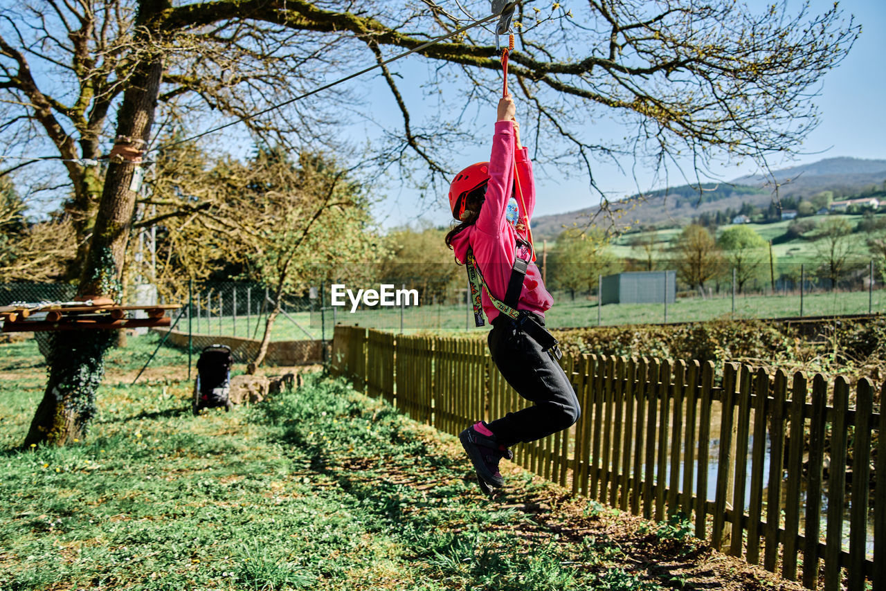 Little girl with protections practicing climbing between trees with ropes and nets