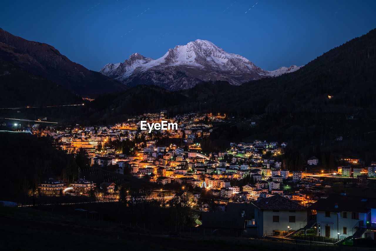 Illuminated town by mountains against sky at night