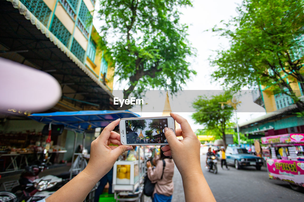 MIDSECTION OF WOMAN PHOTOGRAPHING WHILE USING MOBILE PHONE IN CITY