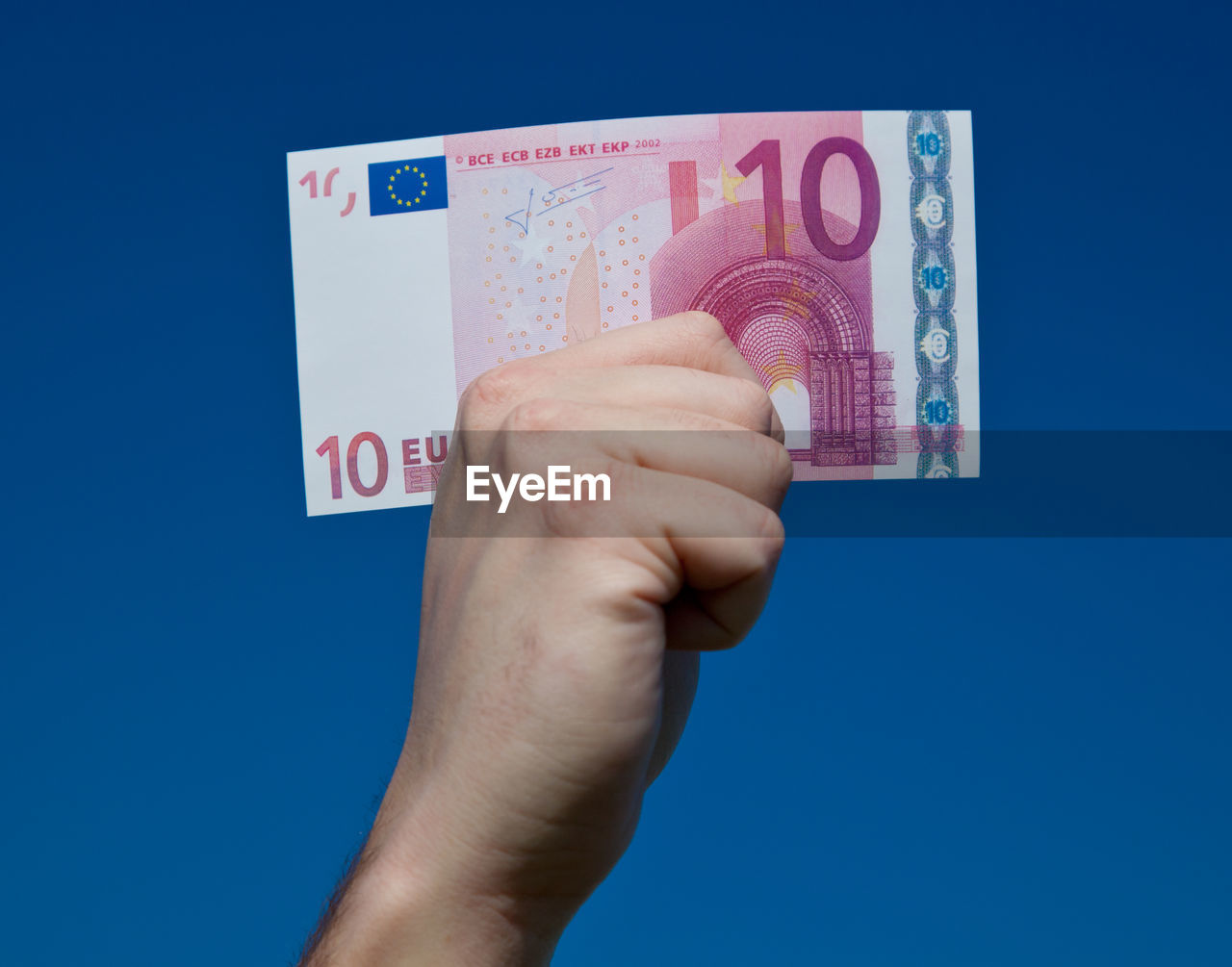 Cropped hand holding ten euro banknote against blue background